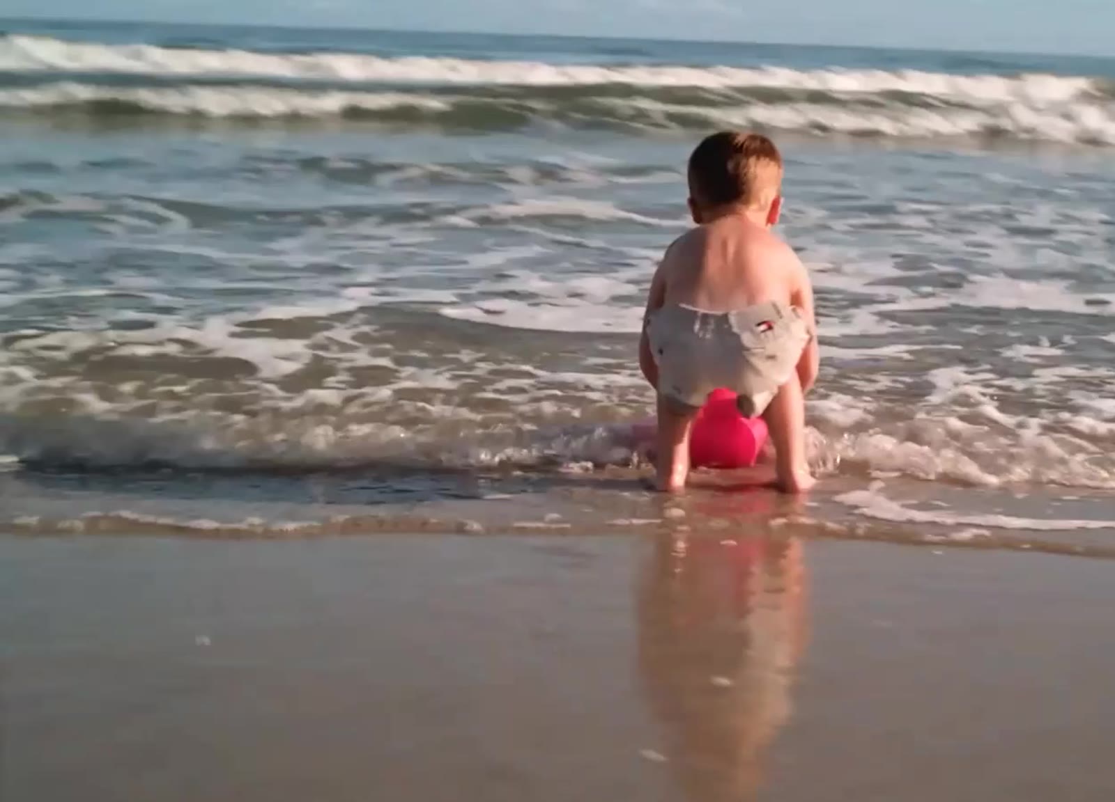 Crianca brincando na beira do mar com ondas ao fundo